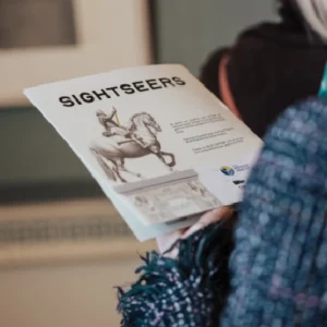 Person reading a brochure about an exhbition called Sightseers